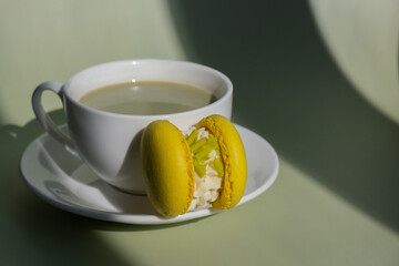 Green latte matcha with yellow macaron dessert on pastel background with creative deep shadows. Concept of holiday breakfast morning tea drink. Cozy minimalist superfood vibrant colors healthy eating