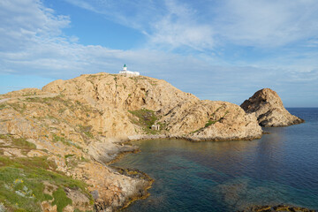 A sunny view of a rocky coastline with a lighthouse. Fanale di Petra, Ile Rousse, Corsica, France.