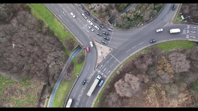 Vehicles passing crossroad in suburbs on cloudy day. Aerial static shot of traffic in town. London, UK