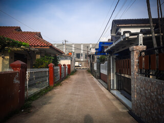 A narrow residential alley under a bright blue sky, flanked by rows of houses with fences