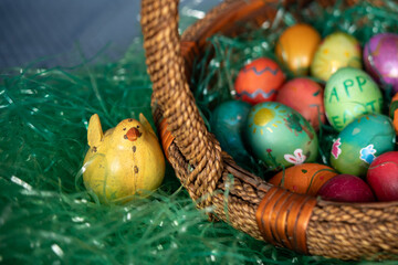 Close up of a yellow chick toy sitting in green plastic grass beside an Easter basket full of colored eggs