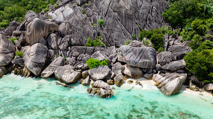 Lush greenery and smooth granite rocks descend into the clear ocean waters at La Digue. Seychelles.