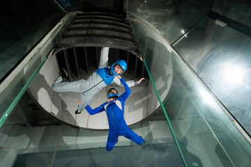 A male instructor teaches a woman how to fly in a wind tunnel. Free fall simulator.