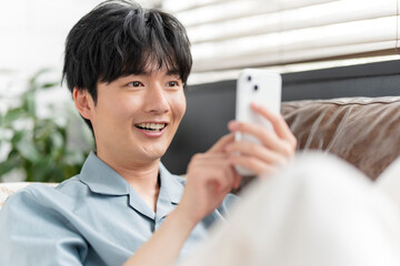ソファーに座りリラックスしながらスマートフォン
の画面を見ている若い日本人男性。