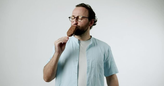A man in a blue shirt indulges in a chocolate ice cream bar on a stick. He savors each bite, clearly enjoying the treat. Simple, satisfying pleasure with a classic frozen dessert. Perfect for summer,