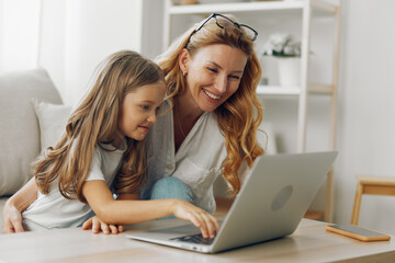 Mother and daughter bonding time on the couch while exploring educational content on a laptop together