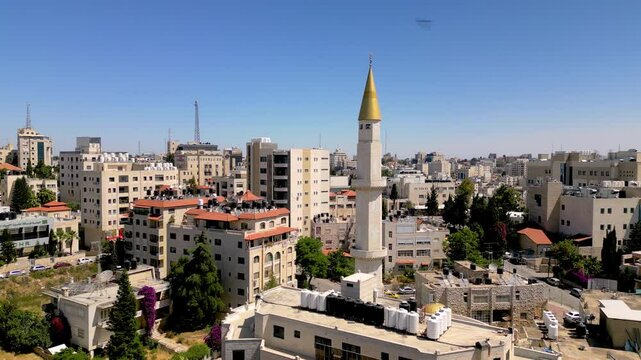 Birds swoop around a landmark golden minaret in Ramallah; view shows the skyline of the capital of Palestine framed against a deep blue sky