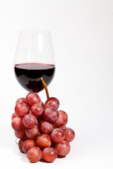 Glass of red wine near a bunch of fresh red grapes on a white background, ready to be enjoyed