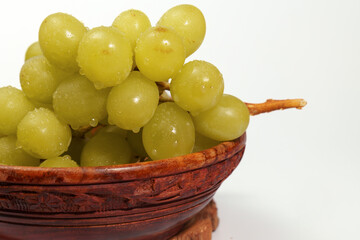 Ripe green grapes with water droplets sit in a wooden bowl, creating a refreshing and healthy image