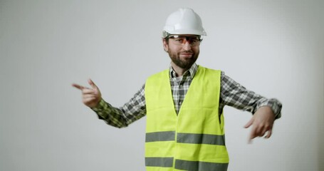 A construction worker wearing a hard hat and safety vest dances in front of a white background. He shows his passion for his profession and enjoys every moment. Great for construction