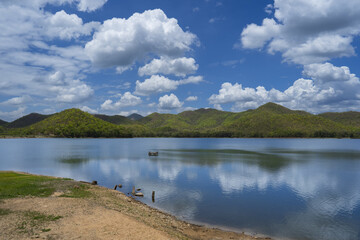 Serene lake surrounded by lush green hills bright blue sky with fluffy white clouds, reflecting beautifully water surface