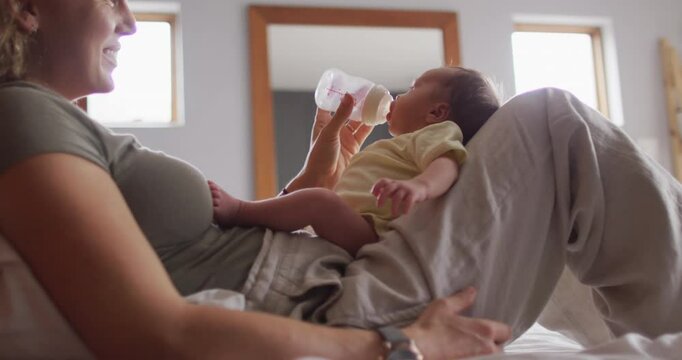 Video of happy caucasian mother feeding newborn baby with bottle on bed