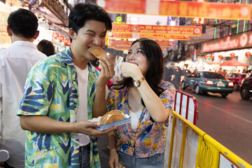 Young Asian couple tourist traveling and eating dessert at Yaowarat China Town in Bangkok Thailand during a holiday