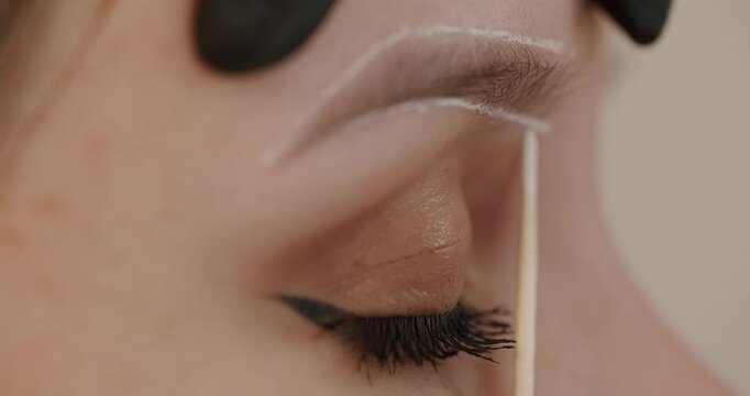 Master applies white markings to correct shape of eyebrows with a special brush. The beautiful face of young girl model on sofa in a beauty salon before microblading, permanent makeup eyebrow tattoo.