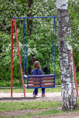 A girl sits on a swing in the park on a spring day