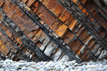 Diagonal stratified rock layers in orange and gray hues with smooth stones below&mdash;ideal for geological textures, abstract visuals, or experimental design backdrops.