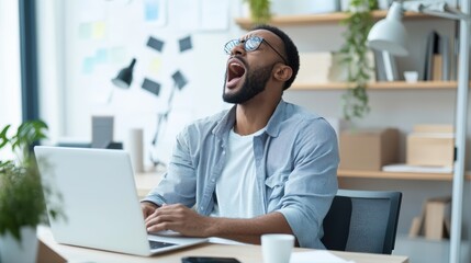 Obraz premium Tired Man Yawning While Working on Laptop in Modern Office Space