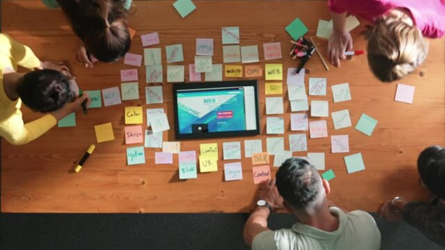 Top down view of programmer brainstorming and planning about web design while looking at tablet wireframe prototype. Aerial view of skilled developer team talking about digital application. Symposium.