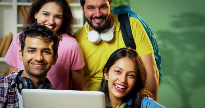 College students celebrating success pointing excitedly at blank space while working on group assignment with laptop, books, notes in friendly college library environment, facing camera together
