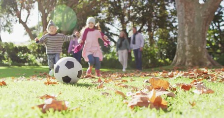 Happy Caucasian siblings kick a football in autumn garden, family strolls behind - Powered by Adobe