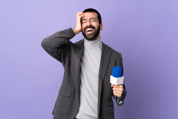 Adult reporter man with beard holding a microphone over isolated purple background laughing