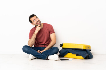 Caucasian handsome man with a suitcase full of clothes sitting on the floor at indoors and looking up