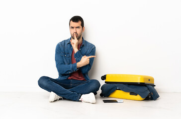 Caucasian handsome man with a suitcase full of clothes sitting on the floor at indoors pointing to...