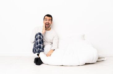 Caucasian man in pajamas sitting on the floor at indoors with surprise and shocked facial expression