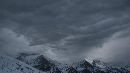 Menacing storm clouds hovering above snow-capped peaks, generating intense atmospheric drama across rugged mountain wilderness under brooding twilight skies - Powered by Adobe