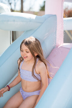 Smiling girl slides down pastel inflatable water slide outdoors.