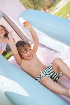 Smiling boy slides down inflatable water slide in sunny backyard