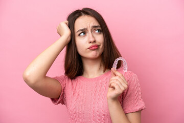 Young Ukrainian woman holding invisible braces isolated on pink background having doubts and with confuse face expression