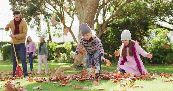 Video of happy caucasian son and daughter throwing autumn leaves while father rakes them up
