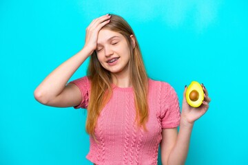 Teenager Russian girl holding an avocado isolated on blue background has realized something and...