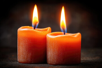 Two orange candles burning brightly in a dark setting, creating a warm, cozy, and peaceful atmosphere.