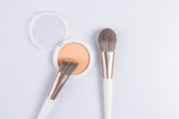 A chic compact powder in a white round package, two white professional makeup brushes on a white background. top view. cosmetic background for design.