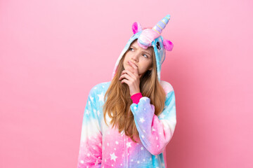 Teenager Russian girl with unicorn pajamas isolated on pink background having doubts and with...