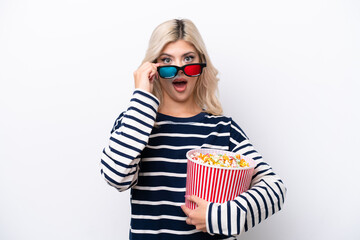 Fototapeta premium Young Russian woman isolated on white background surprised with 3d glasses and holding a big bucket of popcorns