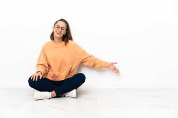 Young woman sitting on the floor extending hands to the side for inviting to come