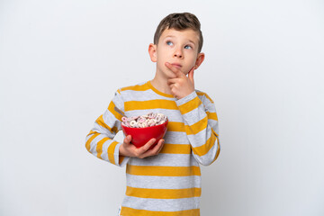 Little caucasian boy holding a cereal bowl isolated on white background having doubts