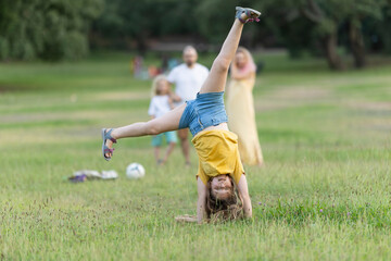 Young girl doing a cartwheel in the park with family watching
