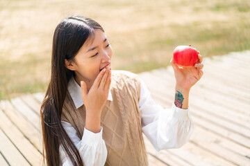 Young Chinese woman with an apple at outdoors with surprise and shocked facial expression