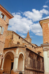 Charm of Urbino medieval streets, the stunning Palazzo Ducale and the majestic bell tower of the Duomo against a vibrant sky. Urbino, Marche region, Italy