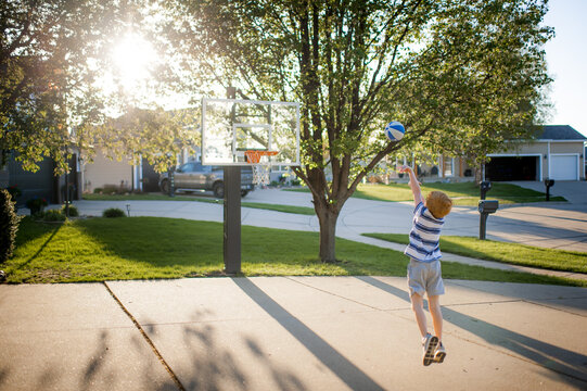 Young boy playing basketball alone on driveway during sunny afternoon