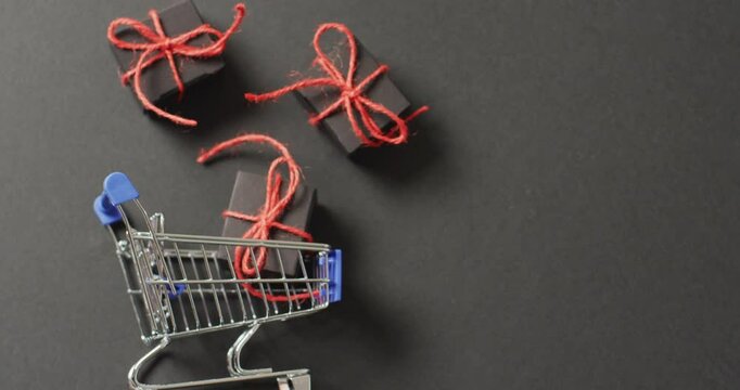Three black gifts tied with red string and shopping cart on black background with copy space