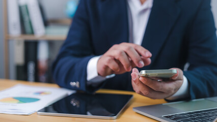 Businessman using smartphone for digital communication or financial analysis at office desk, representing mobile productivity, Technology in business, and online data management.