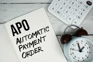APO Automatic Payment Order text on paper notebook page with alarm clock and calculator on wooden...