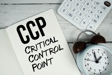 CCP Critical Control Point text on paper notebook page with alarm clock and calculator on wooden background