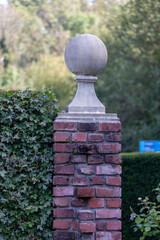 Historic Stone Finial on Brick Pillar with Ivy Growth in Garden