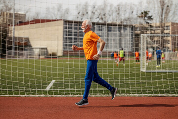 Side view of an old sporty man running on stadium.